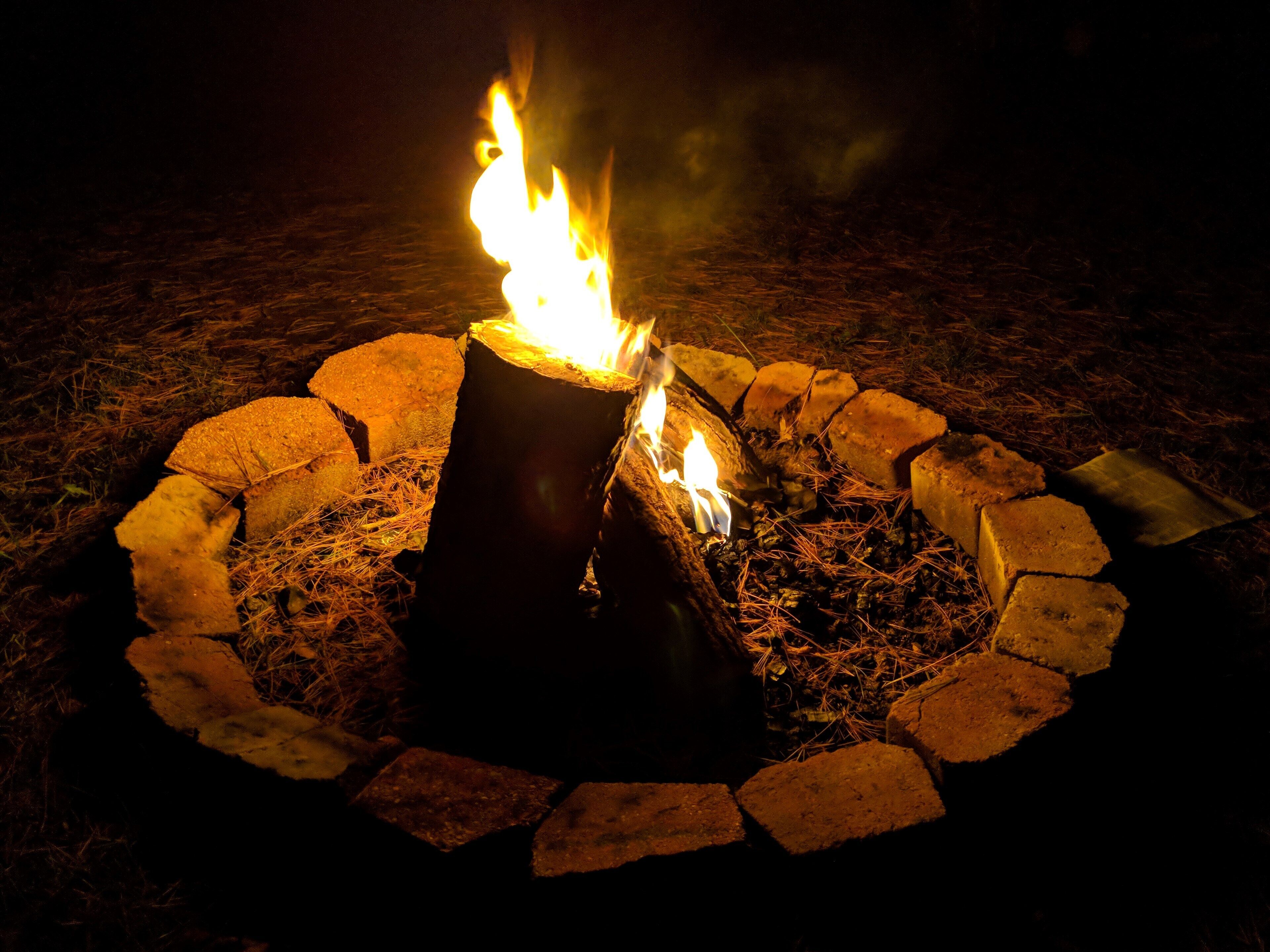 Un feu de camp avec des bûches et des pierres disposées en cercle, entouré d’herbe sèche.
