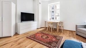 A modern living room with a flat-screen TV, a wooden dining table, a grey sofa, and a patterned rug. - WeHost Oikokatu 15 (Helsinki)