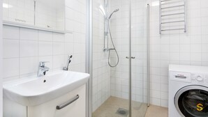 A bathroom with a sink, mirror, shower, and a washing machine. - WeHost Oikokatu 15 (Helsinki)