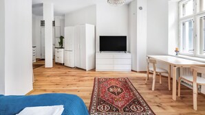 A modern bedroom with a large bed, a TV, a dining area, and a kitchen in the background. - WeHost Oikokatu 15 (Helsinki)