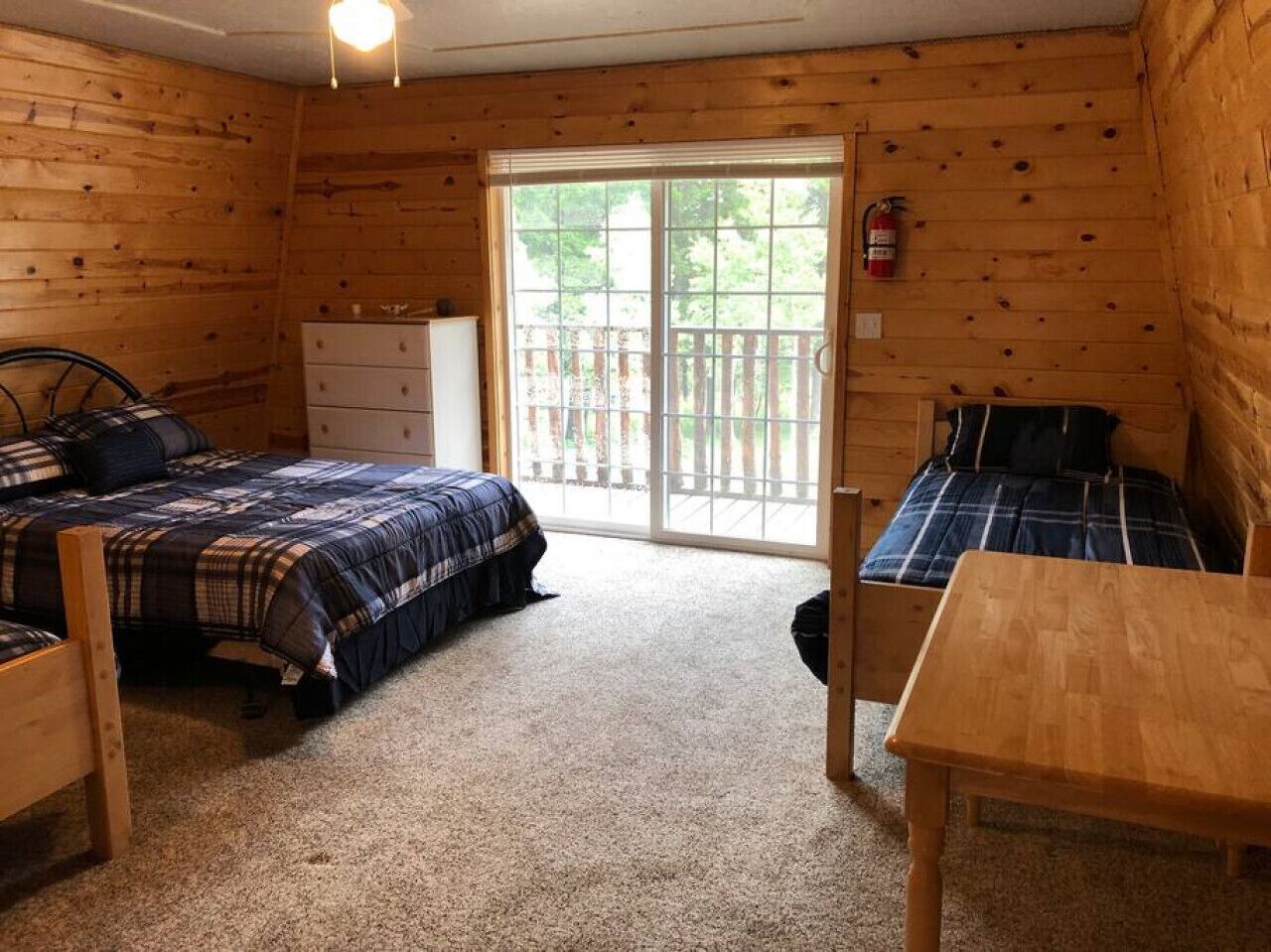 A cabin-style room with two beds, a wooden table, and a sliding glass door leading to an outdoor deck.