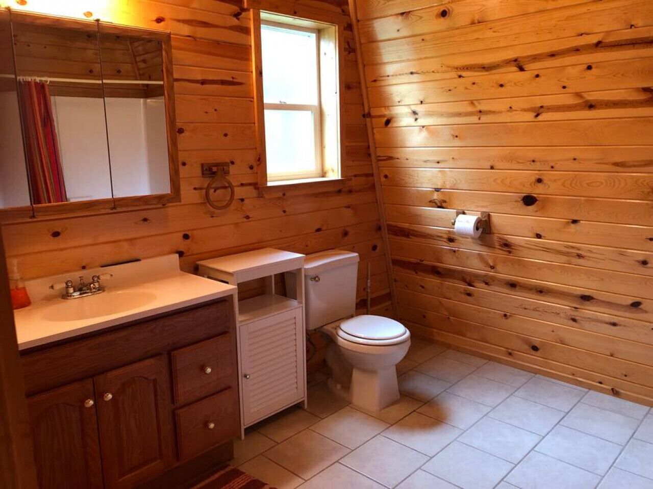 Une petite salle de bain aux murs lambrissés, équipée d’un lavabo, de toilettes et d’un miroir.