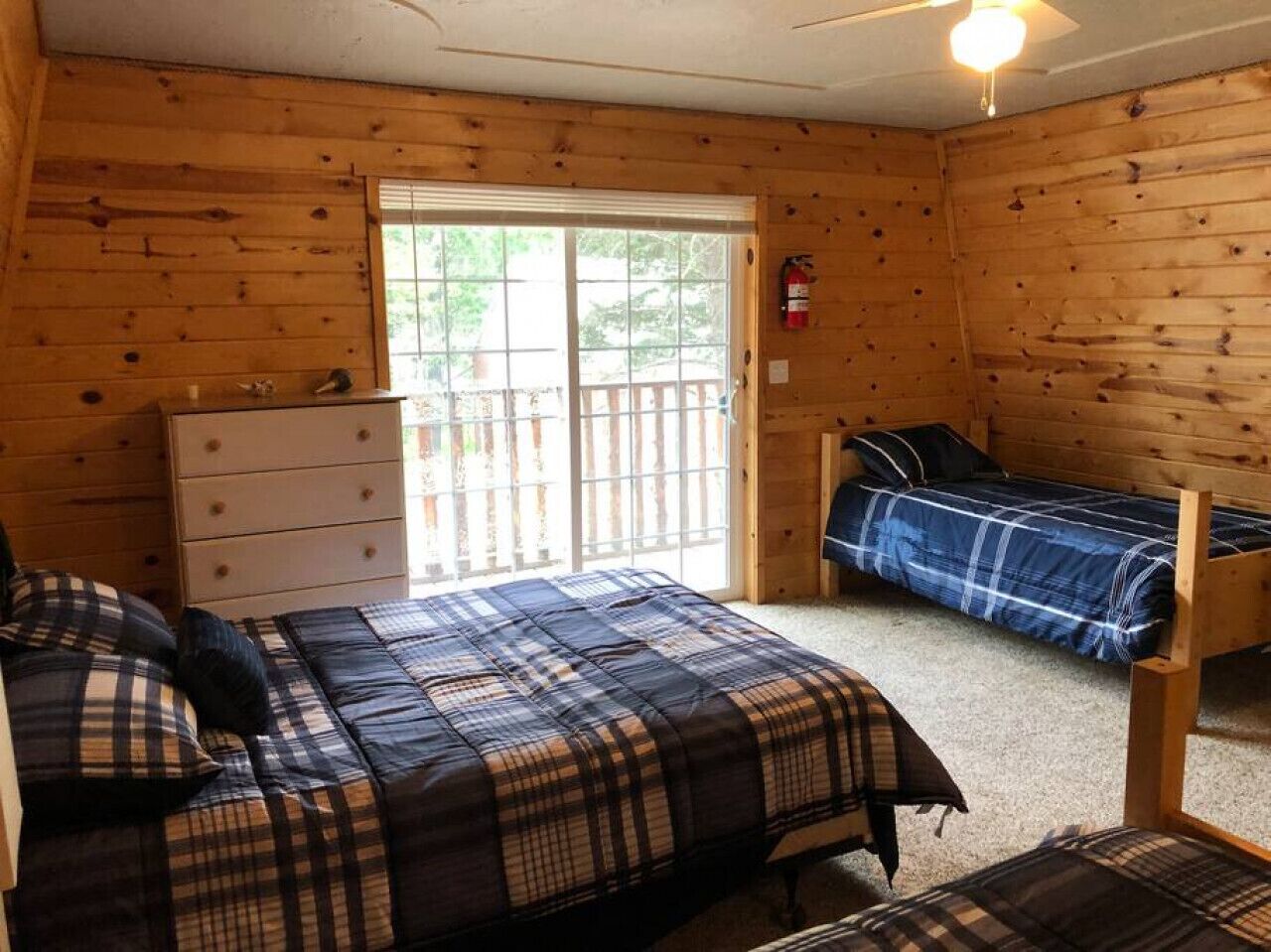 Ein schlicht eingerichtetes Schlafzimmer mit einem großen Bett, einem Einzelbett, einem Schminktisch und einer Schiebetür zu einer Außenterrasse.