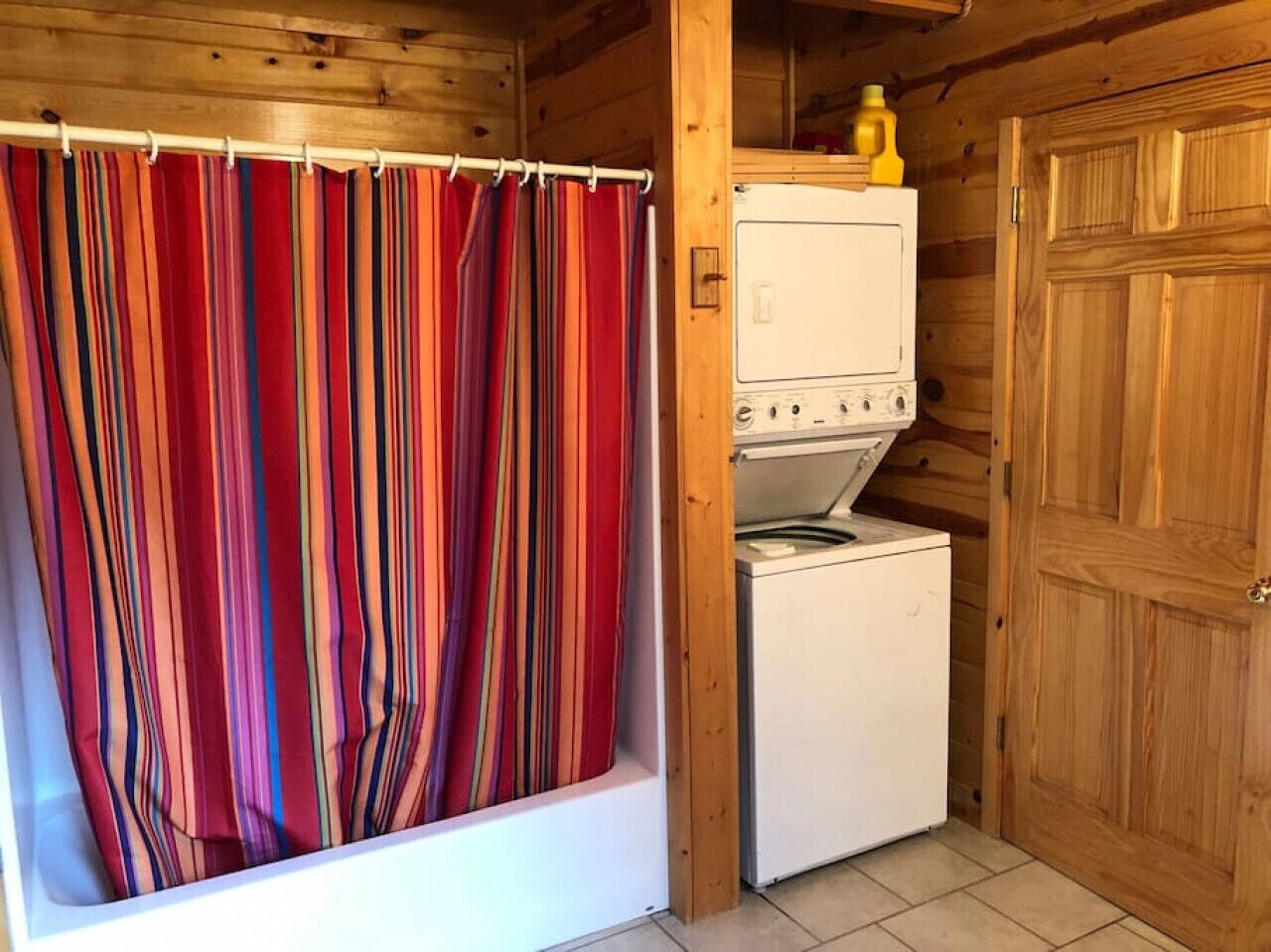 Une petite cabane en bois avec un rideau de douche, un lave-linge et une porte en bois.
