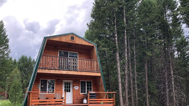 A two-story log cabin with a balcony, surrounded by tall pine trees. - Balcony, 20 min to Yellowstone, Sled/ATV Spot (Island Park)