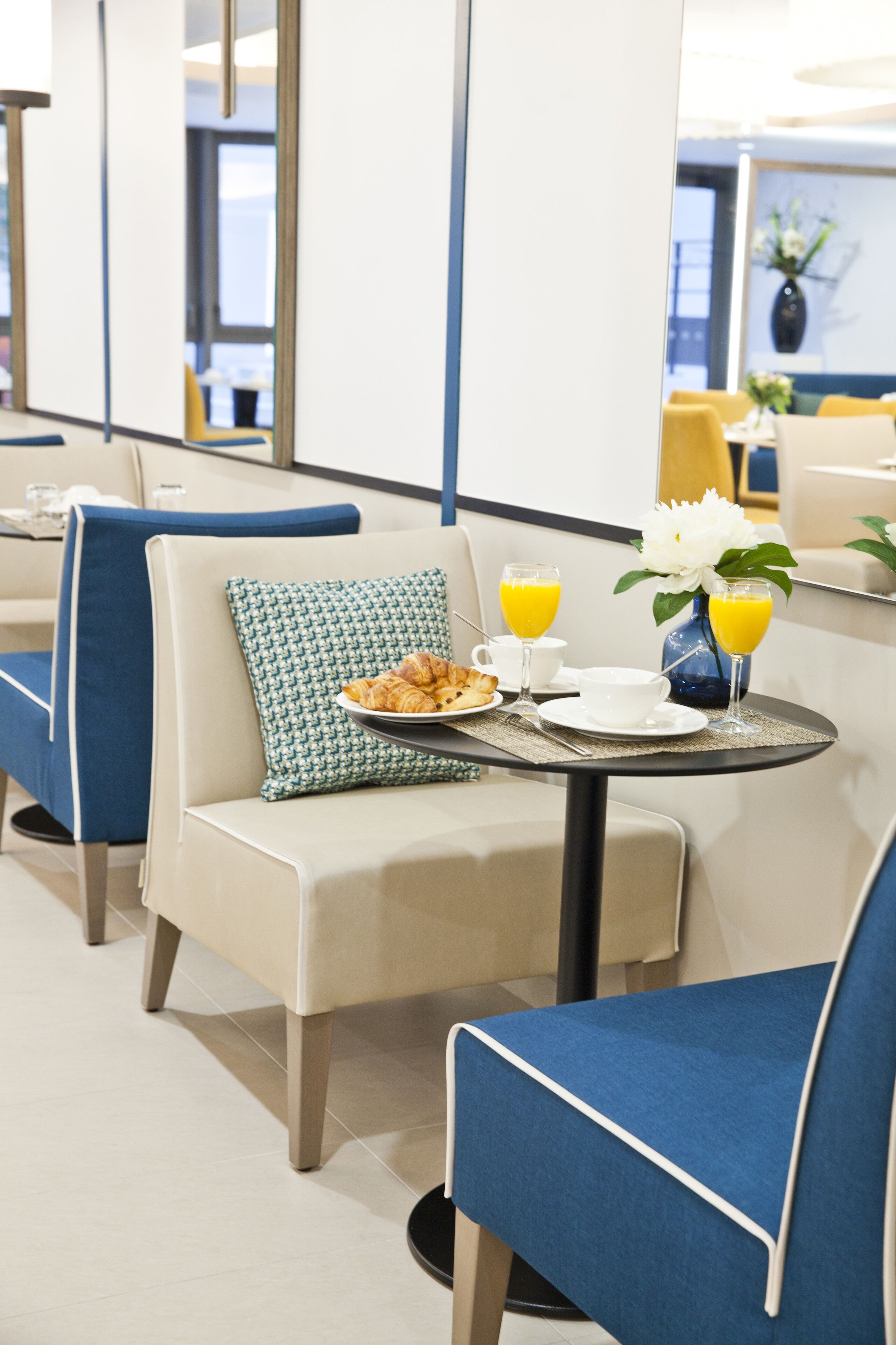 Habitación de hotel con comedor, mostrando una mesa dispuesta con alimentos para el desayuno, como croissants, una taza y un jarrón con flores.