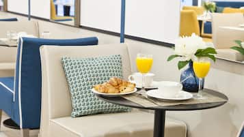 Habitación de hotel con comedor, mostrando una mesa dispuesta con alimentos para el desayuno, como croissants, una taza y un jarrón con flores.