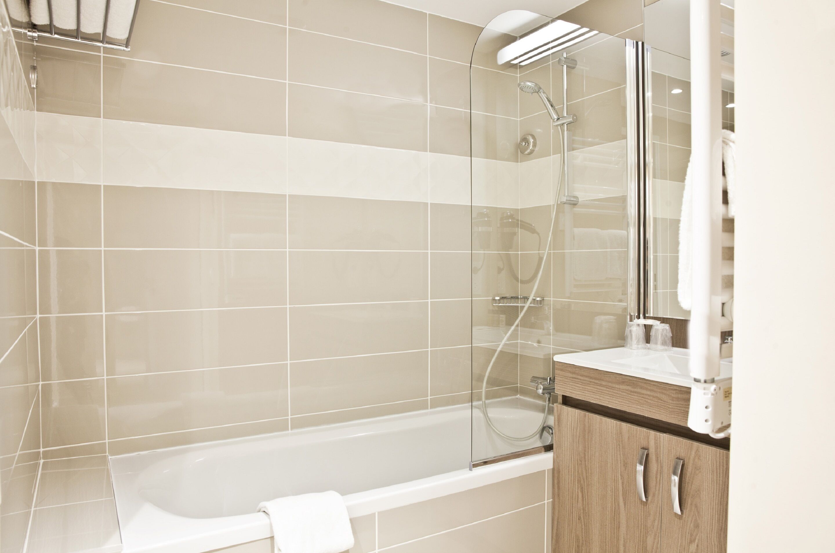 A modern bathroom with a glass-enclosed shower, a white bathtub, and a wooden vanity with a mirror.
