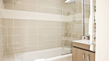A modern bathroom with a glass-enclosed shower, a white bathtub, and a wooden vanity with a mirror.