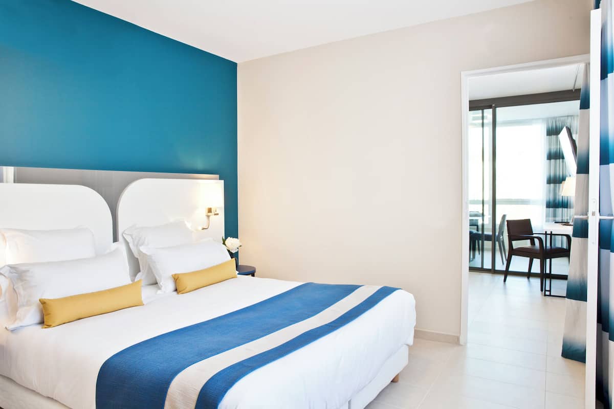 A modern hotel room with a large bed, a view of the balcony, and a separate dining area.