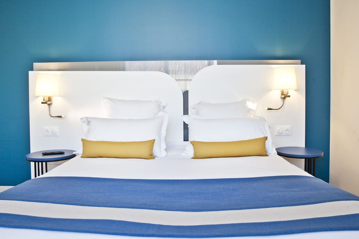 A double bed with white and gold pillows, a blue and white striped bedspread, and two bedside tables with lamps.