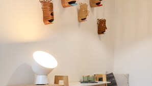 Un bureau en bois, une lampe blanche, une chaise et une petite table sur laquelle se trouvent des livres et une bougie.