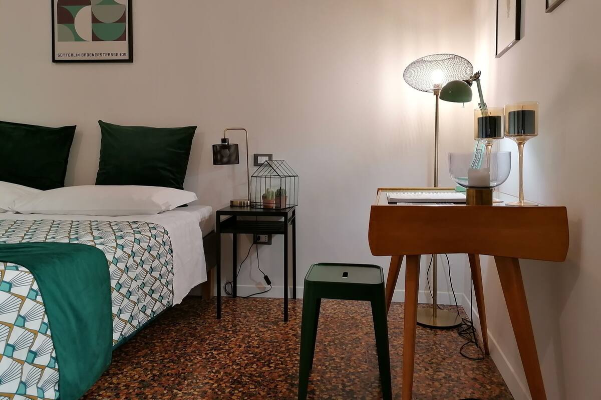 A neatly arranged hotel room with a bed, bedside table, lamp, and a small stool.