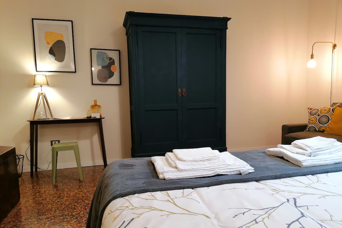 A neatly made bed with folded towels, a desk with a lamp, and two framed abstract artworks on the wall.