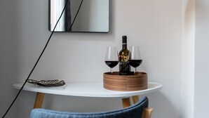Une table ronde en bois, sur laquelle sont posés une bouteille de vin et deux verres, est placée sur une table blanche, adossée à un mur orné d’un miroir.