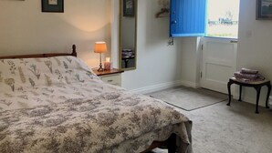 Ein Schlafzimmer mit einem Bett, einem Nachttisch mit Lampe, einem Spiegel, einer blauen Tür und einem kleinen Tisch mit Handtüchern.