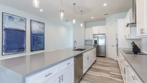 A modern kitchen with white cabinets, stainless steel appliances, and a marble countertop. - Modern Beach House for 24! Private Pool, Ocean Views, & Directly Across from Beach! (South Padre Island)