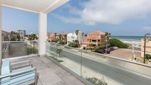 A balcony with a clear view of the beach and ocean, a parking area, and residential buildings. - Modern Beach House for 24! Private Pool, Ocean Views, & Directly Across from Beach! (South Padre Island)