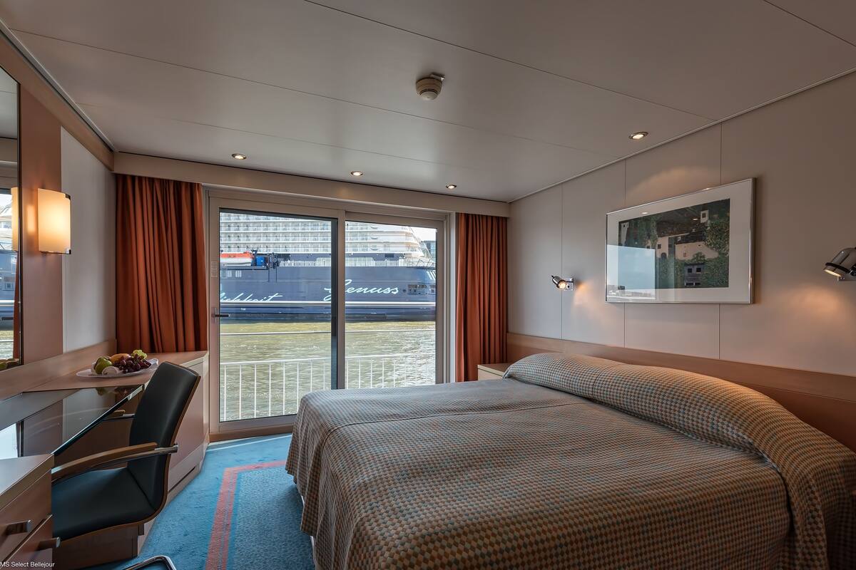 Une chambre d’hôtel avec un lit, un bureau et une chaise, une fenêtre avec des rideaux et un tableau encadré au mur.