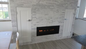 Et moderne køkken med indbygget pejs, hvide skabe og en backsplash i grå fliser.