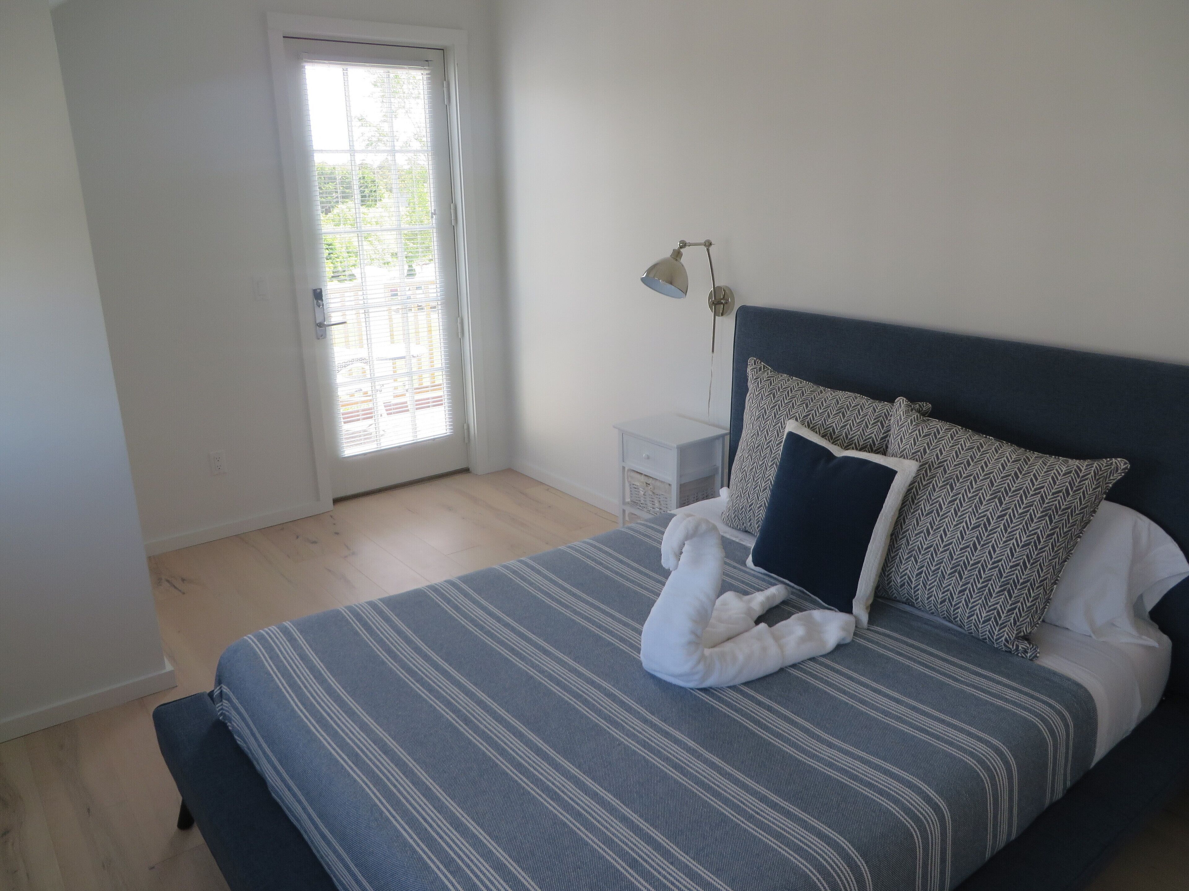 Ein Schlafzimmer mit Bett, Nachttisch, Lampe und einer Tür mit Blick ins Freie.