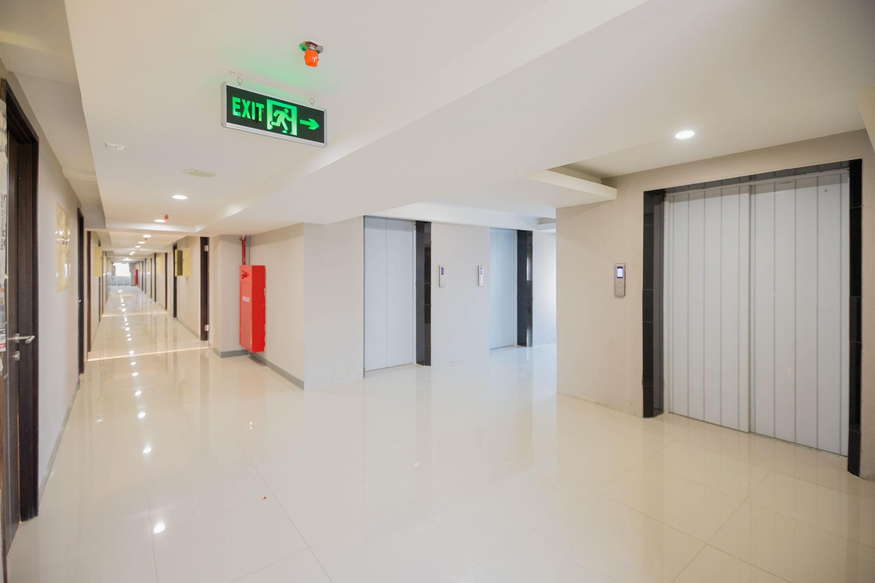 A clean, modern hallway with an exit sign, a fire extinguisher, and a door with a handle.