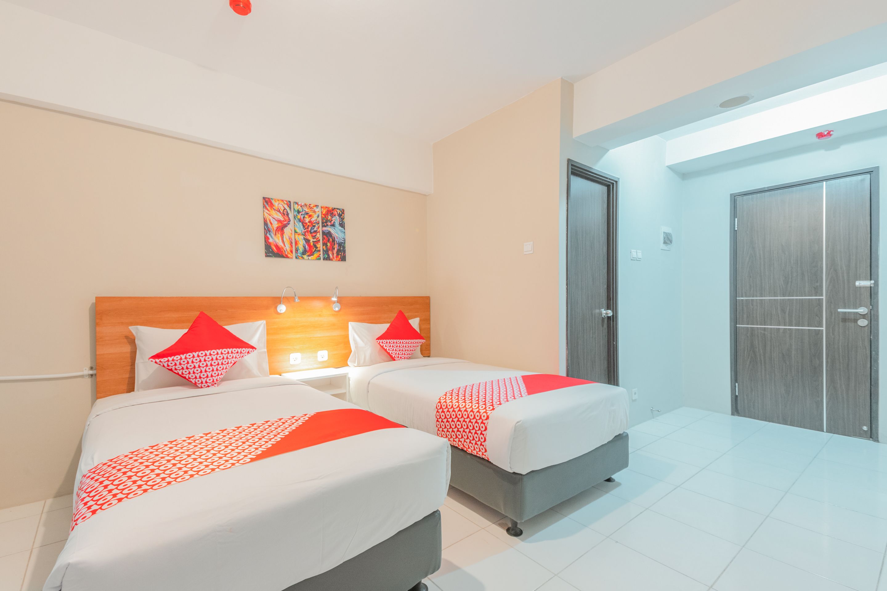 Une chambre d’hôtel avec deux lits, une tête de lit en bois, un tableau au mur et une porte sur le côté droit.