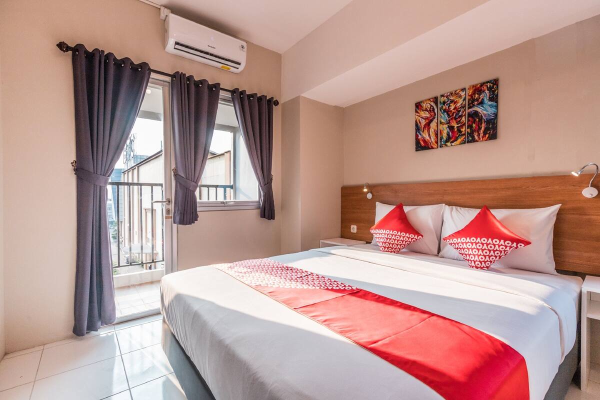Ein Hotelzimmer mit Bett, Vorhängen, einer Klimaanlage, einem Gemälde und einem Balkon.