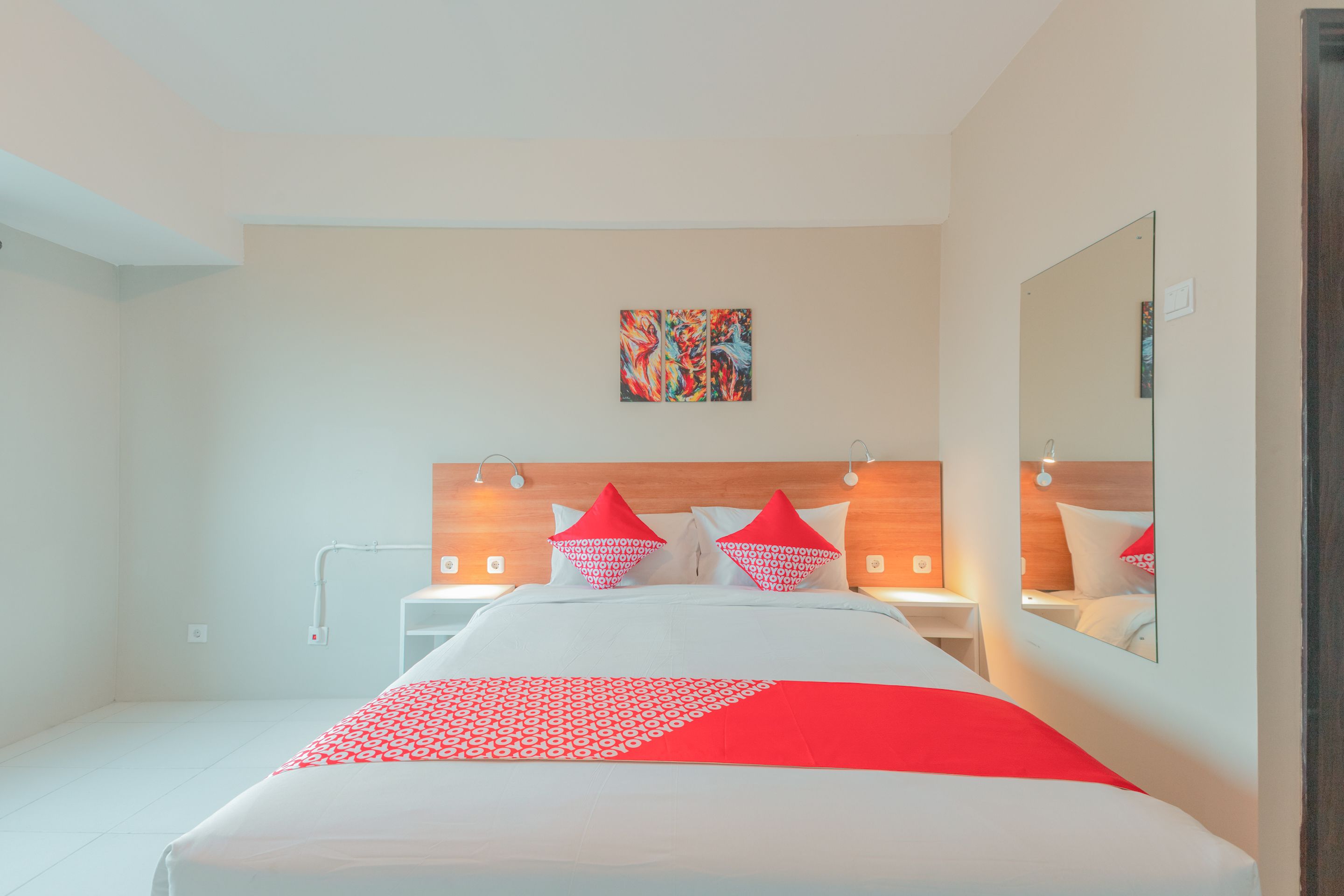 A modern hotel room with a large bed, a headboard with integrated lighting, a bedside table, and a mirror.