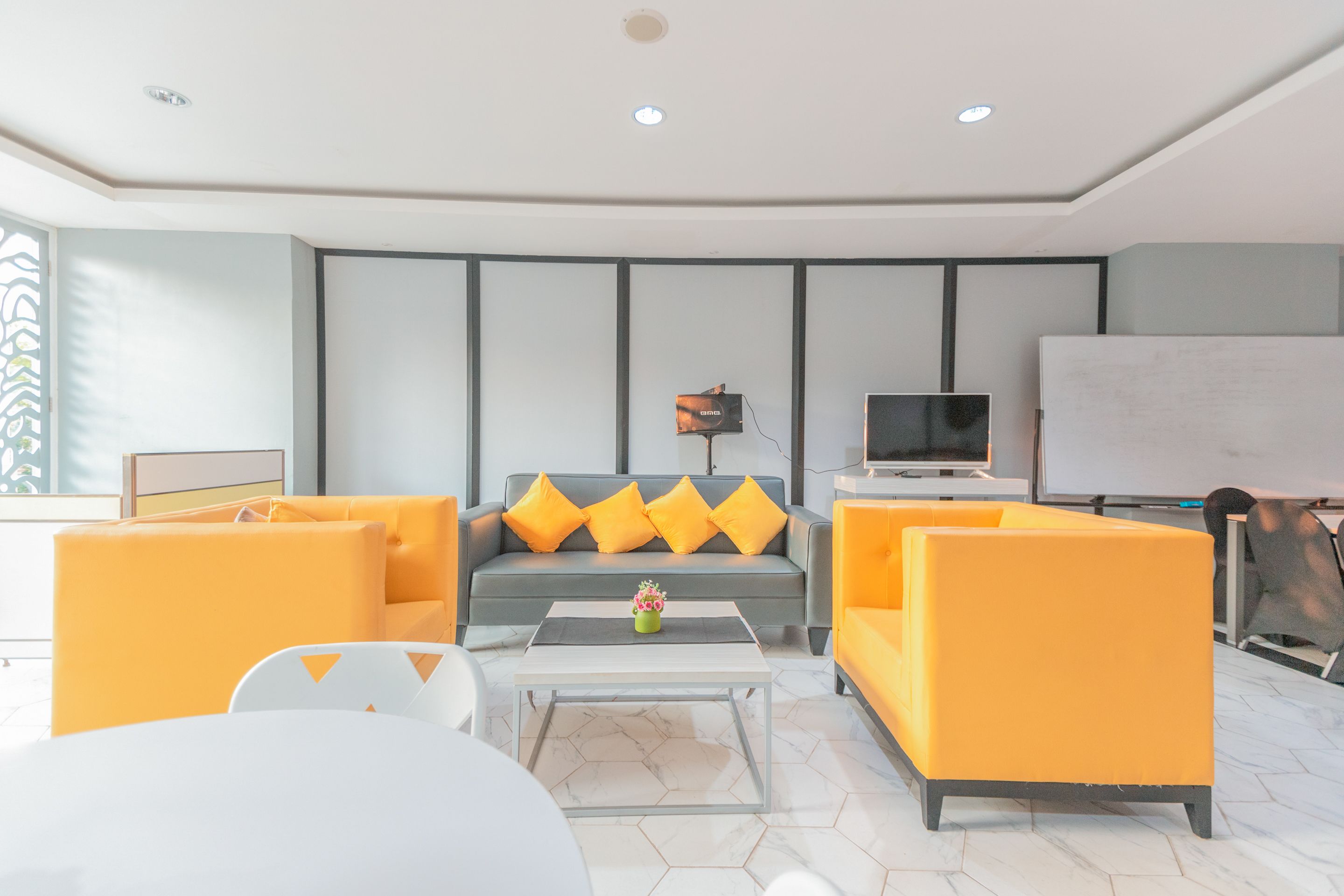 A modern living room with a grey sofa, yellow cushions, a white coffee table, and a flat-screen TV.
