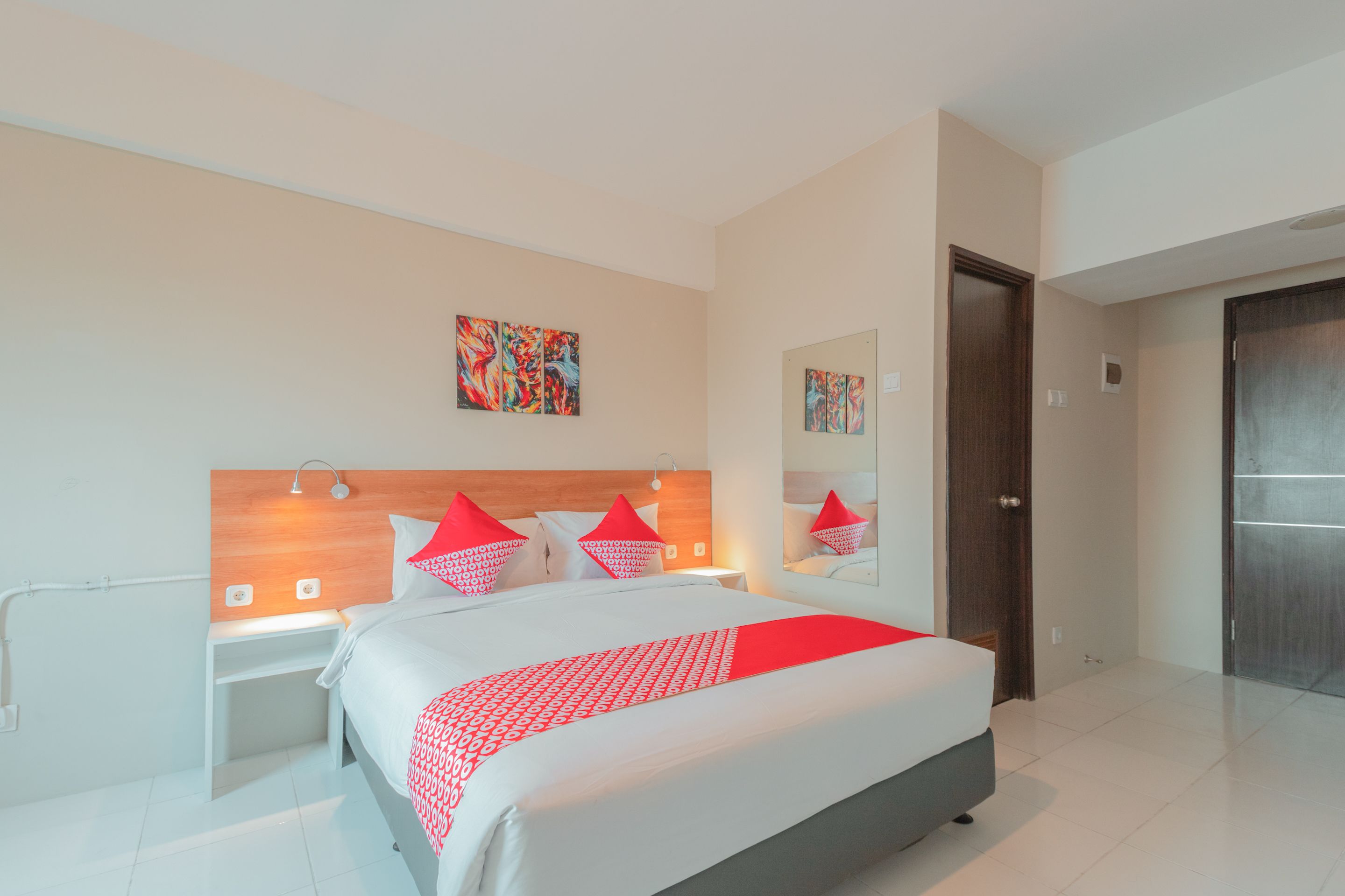 A modern hotel room with a large bed, a wooden headboard, and a nightstand with a lamp.