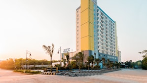 Un hôtel à plusieurs étages, reconnaissable à son grand panneau « BTC », entouré de palmiers et bordé d’une zone pavée.