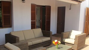 Un patio con mobiliario de mimbre, una mesa con cubierta de vidrio y un florero con flores.