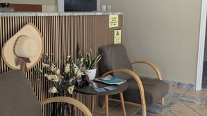 A reception area with a reception desk, framed pictures, a chair with a hat, a small table with a vase of flowers, and a tiled floor. - Grapevines Hotel (Zakynthos)