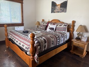 A wooden bed with patterned bedding, a nightstand with a lamp, and a window with blinds. - 2BR, 1B, Sleeps 4, Lakeview and Lake access in West Glacier (West Glacier)
