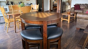 A dining area with a wooden table and chairs, a chessboard, and a kitchen in the background. - 2BR, 1B, Sleeps 4, Lakeview and Lake access in West Glacier (West Glacier)