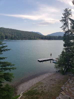 En stilla sjö med en brygga som sträcker sig ut i vattnet, omgiven av tät skog och berg i bakgrunden.