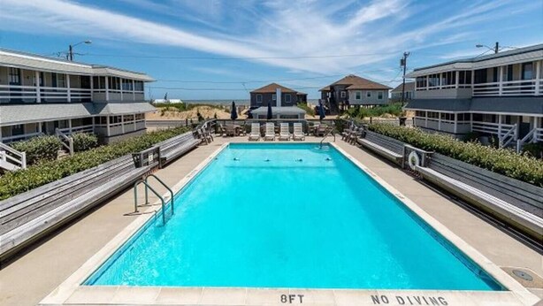 A rectangular swimming pool with a no diving sign, surrounded by lounge chairs and a wooden deck.