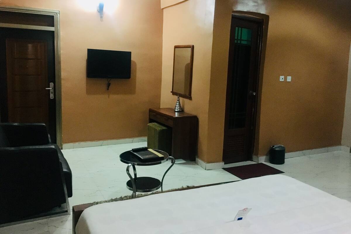 Habitación de hotel con cama, escritorio con lámpara, televisor, silla y cubo de basura.