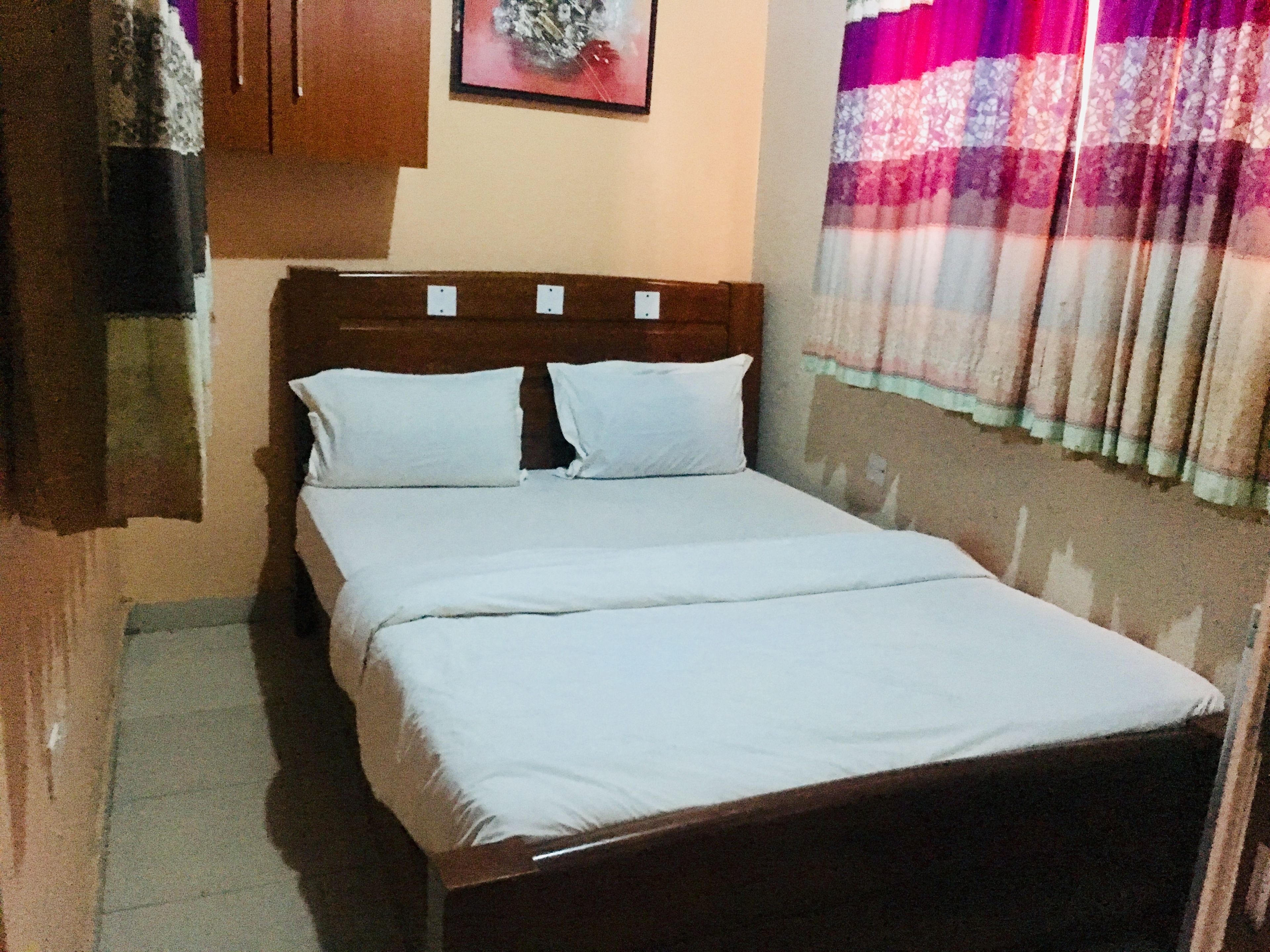 A single bed with a wooden headboard, white bedding, and a wall-mounted picture.