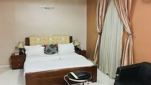 A hotel room with a bed, bedside tables, a lamp, a small table with a remote control, and a black sofa. - Euc Demodern Hotel & Suites (Lagos)