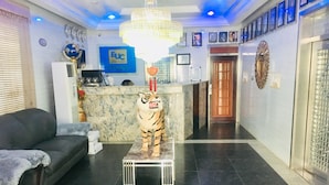 A lobby with a tiger statue on a platform, a grey sofa, a reception desk, and a blue sign with 'EUC' on the wall. - Euc Demodern Hotel & Suites (Lagos)