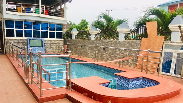 A swimming pool with a red and blue tiled design, surrounded by a metal railing and a stone wall. - Euc Demodern Hotel & Suites (Lagos)