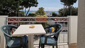 Ein Balkon mit Tisch und Stühlen, mit Blick auf eine Küstenlandschaft mit Bäumen und Gebäuden.