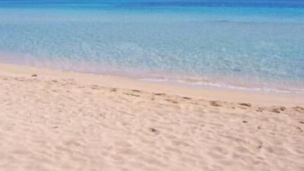 Ein Strand mit klarem, blauem Wasser und sandigem Ufer.