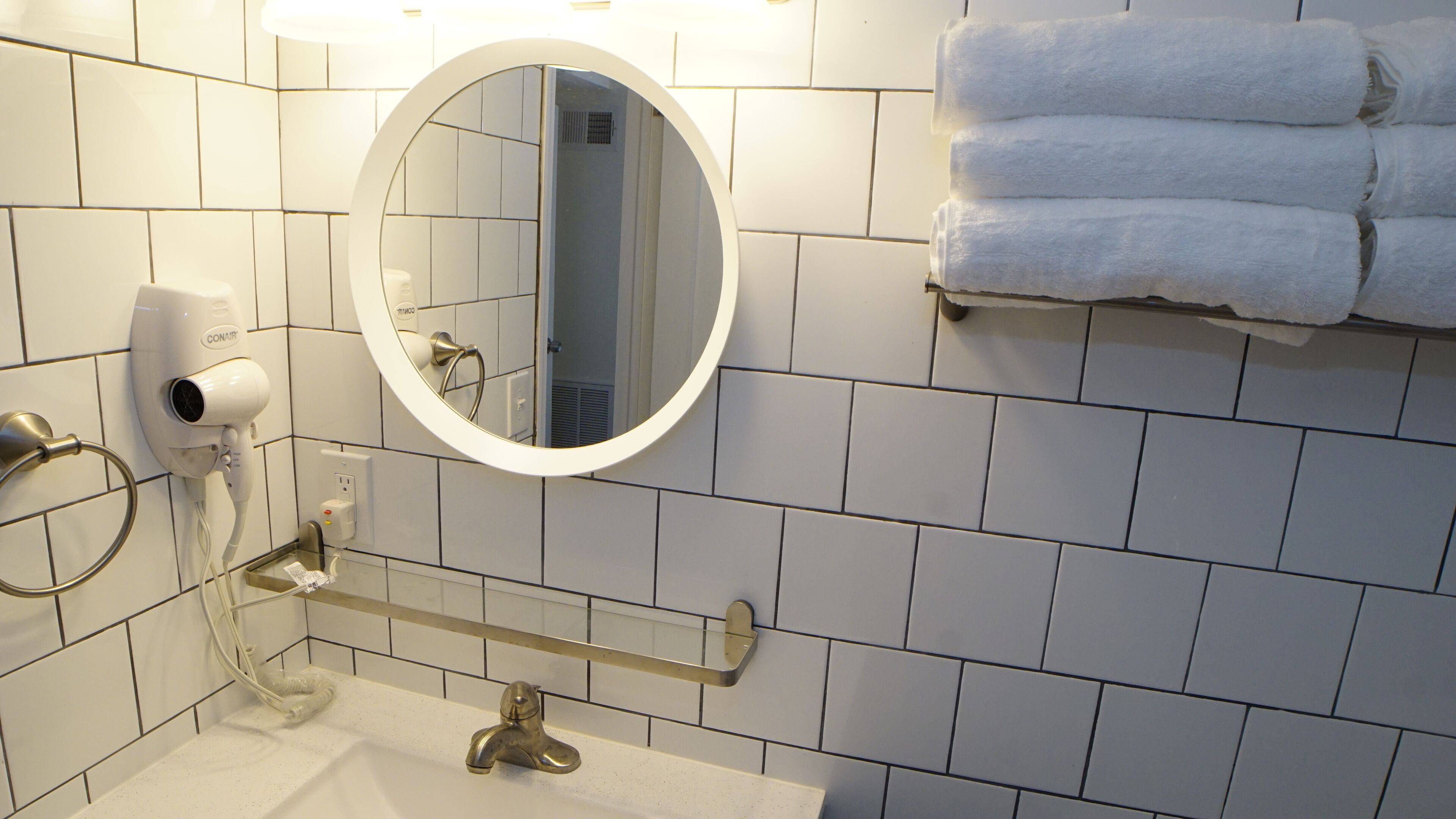 A bathroom with a white sink, a round mirror, a towel rack with towels, and a hairdryer.