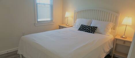 A neatly made bed with white linens, two bedside tables with lamps, and a window with blinds.