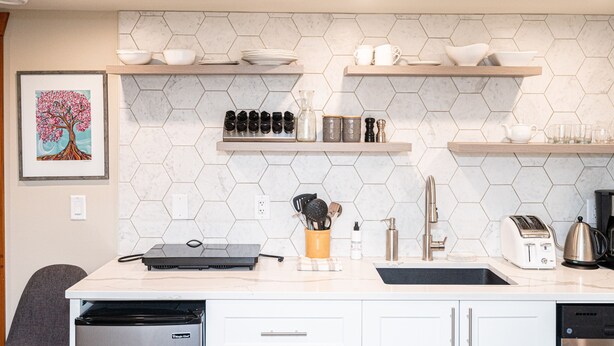 Una cocina moderna con armarios blancos, un salpicadero de mármol y estantes de madera con vajilla y utensilios.