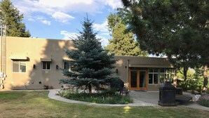 Un edificio con un árbol grande en el jardín delantero, un patio con mobiliario exterior y una chimenea.