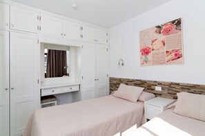 A bedroom with two beds, a dresser, a vanity with a mirror, and a wall-mounted artwork.